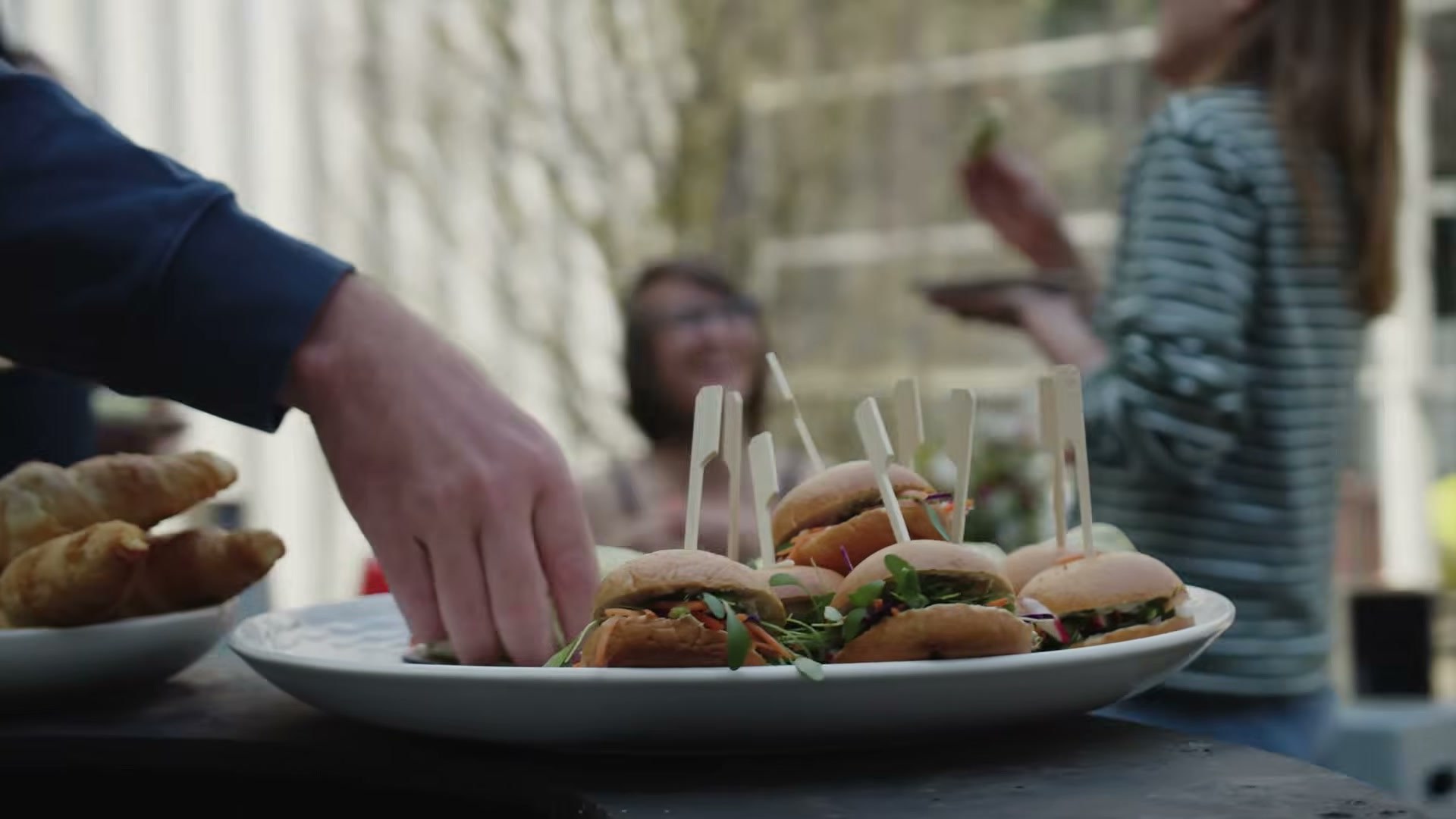 Een bord met kleine broodjes met prikkers, gasten nemen ervan