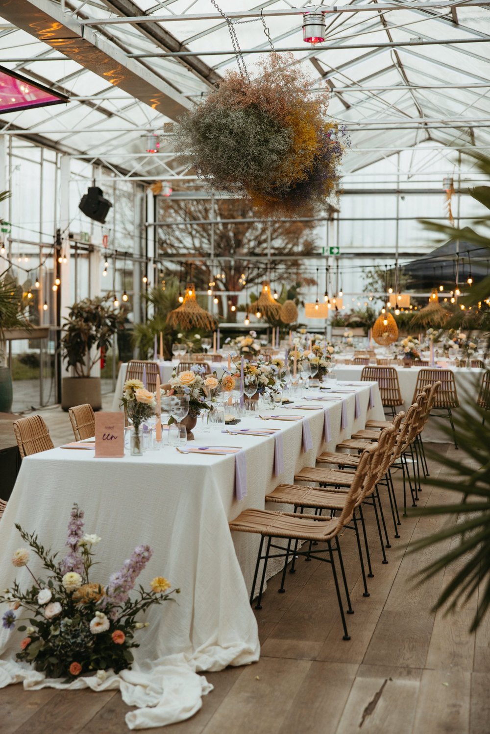 Een lange gedekte tafel met witte tafellakens en veldbloemen in de serre